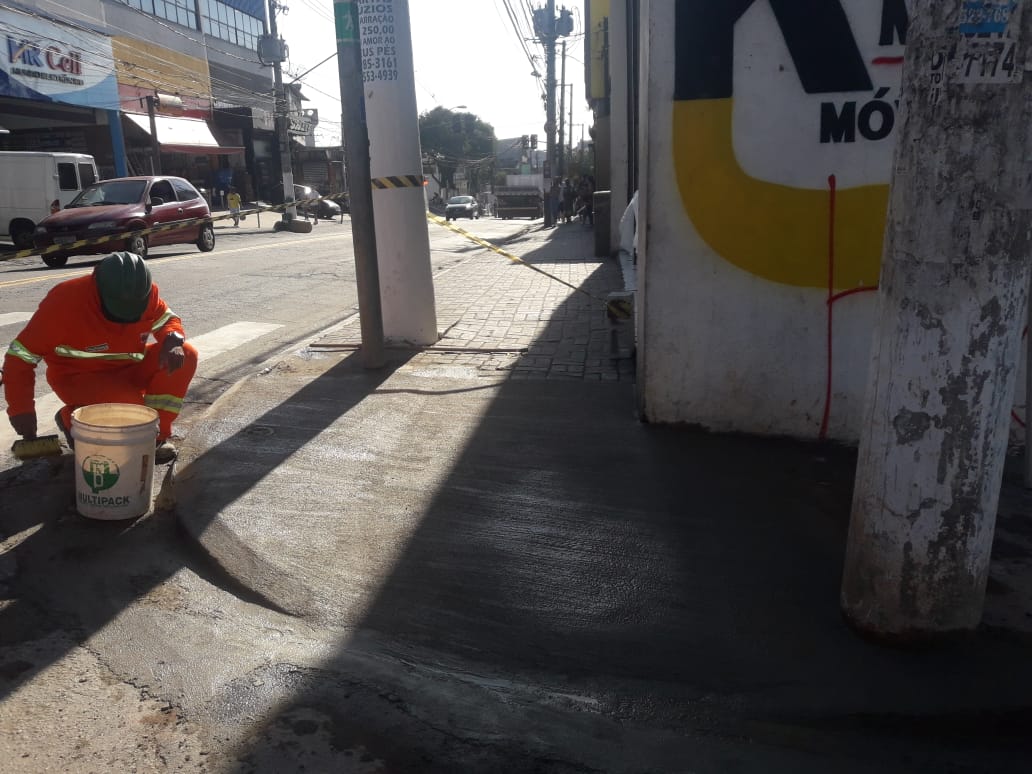 imagem mostra funcionário vestido com uniforme laranj abaixado, terminando de reformar a rampa de acessibilidade