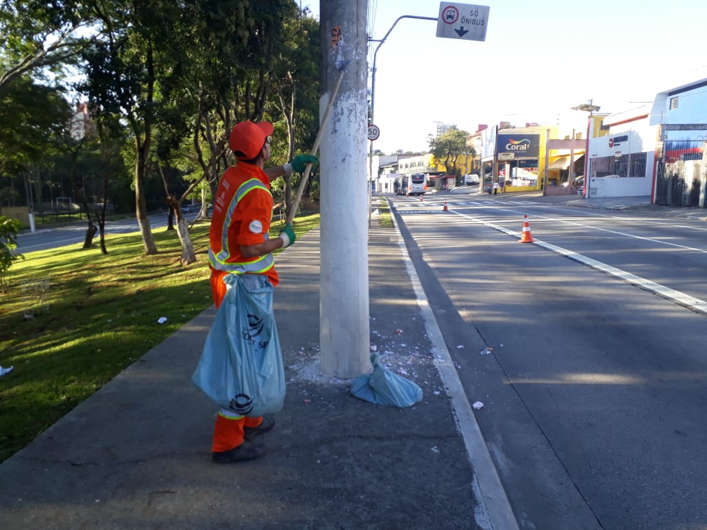 Imagem mostra funcionário vestido de laranja raspando propaganda irregular de um poste