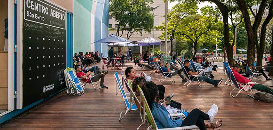 Foto colorida do Centro Aberto do Largo São Bento com pessoas sentadas nas cadeiras