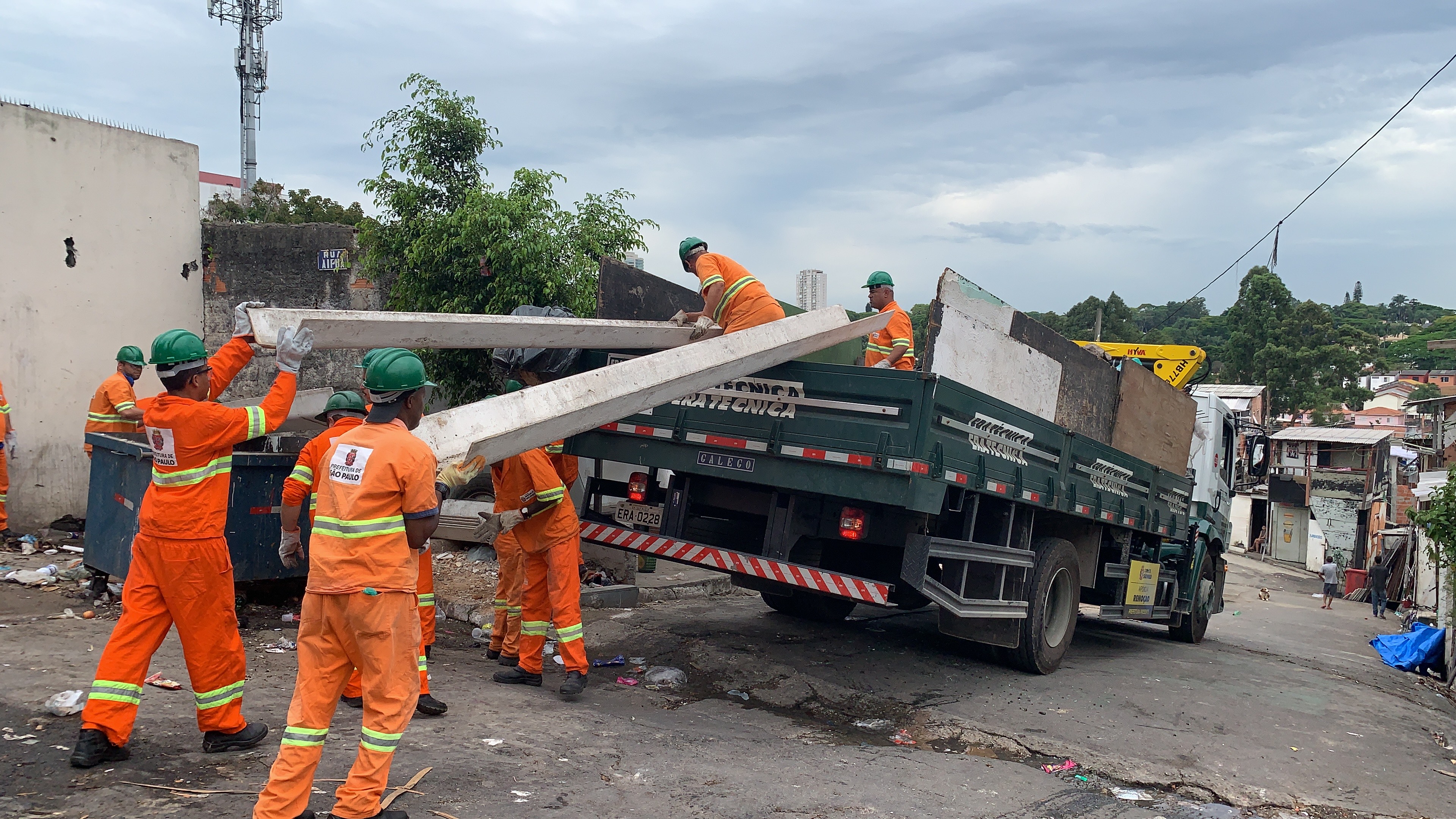 Imagem colorida mostra agentes de zeladoria da Subprefeitura Santo Amaro executando os serviço de limpeza e removendo entulho e o colocando em uma caminhão.