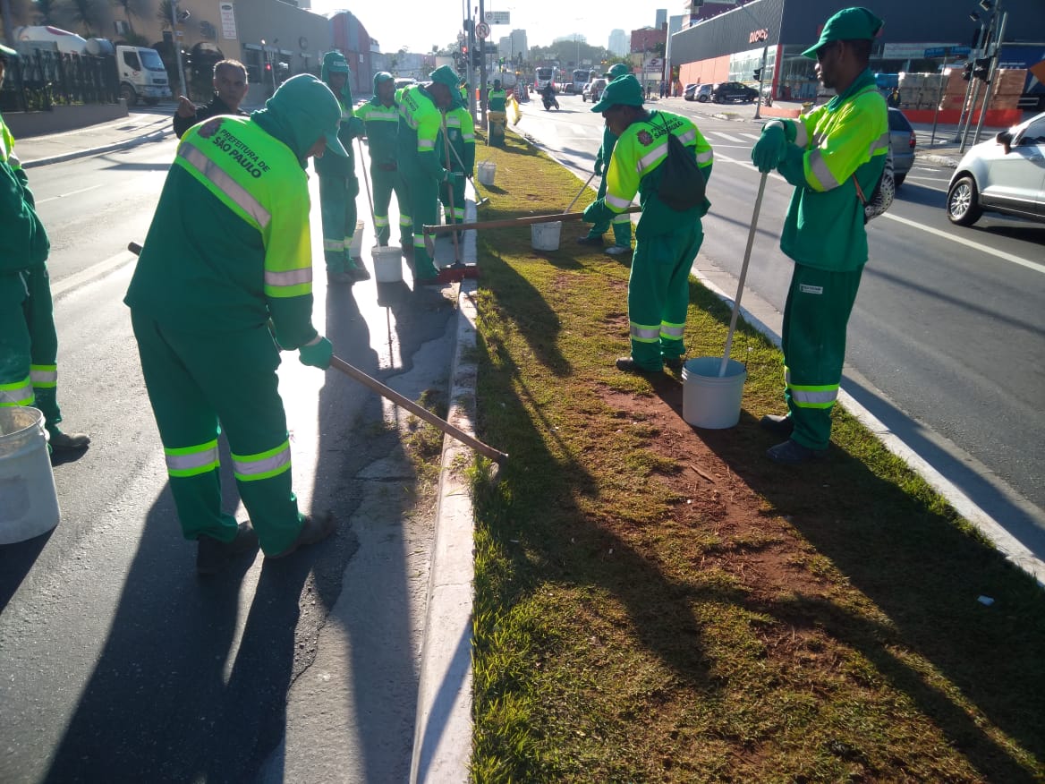 Funcionários da Prefeitura, vestidos de verde, fazem a roçagem e pintura de uma guia localizada na Avenida João Dias