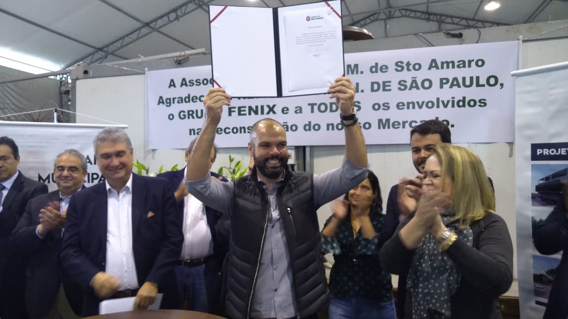 Foto colorida mostra o prefeito de São Paulo, Bruno Covas, segurando o contrato de concessão do Mercado de Santo Amaro ao lado de outras autoridade públicas.