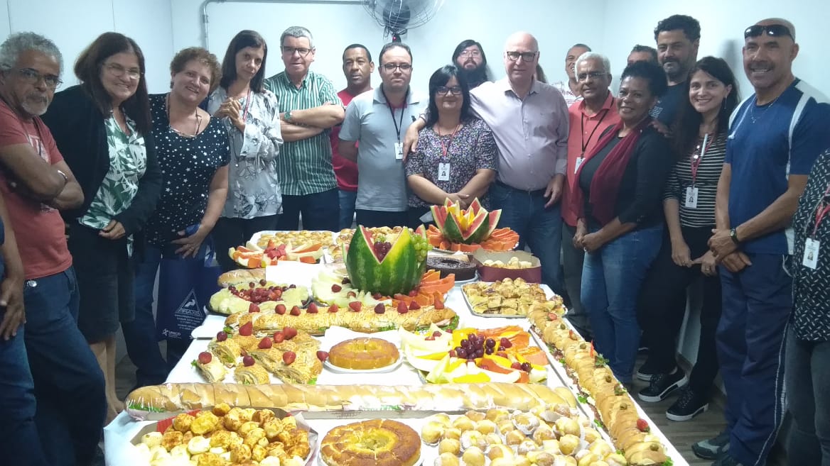 Imagem mostra os funcionários da Subprefeitura Santo Amaro em volta de uma mesa com alimentos em comemoração ao dia do servidor.