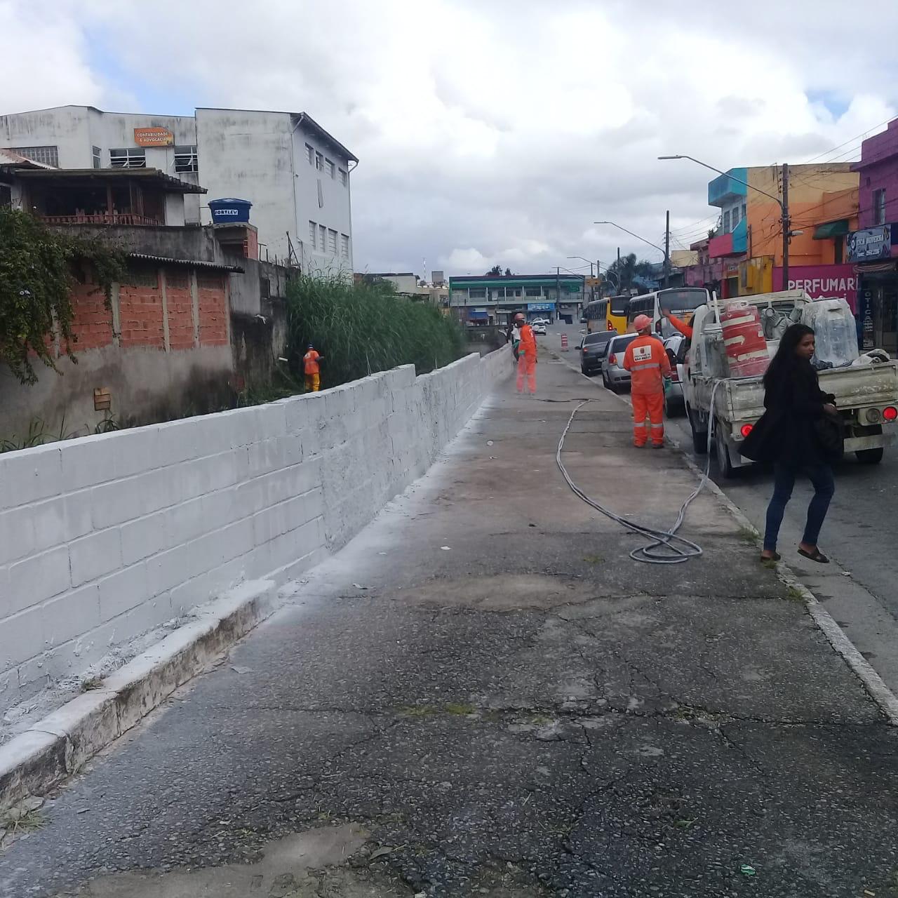 Funcionários de uniforme laranja pintando o muro do córrego