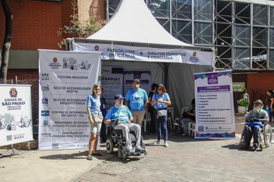 Tenda branca com quatro pessoas  com camisetas azul em frente da tenda