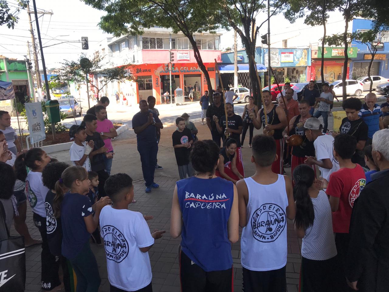 Roda de capoeira, pessoas tocando instrumentos e uma dupla agachada