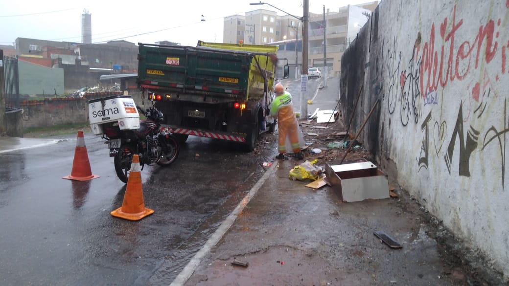 Caminhão estacionado e homem uniformizado de verde retirando o lixo da rua
