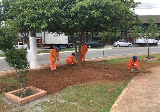 Equipe de serviços com uniforme laranja realiza plantio de gramado em canteiro da praça Dona Graça em frente ao terminal Cidade Tiradentes