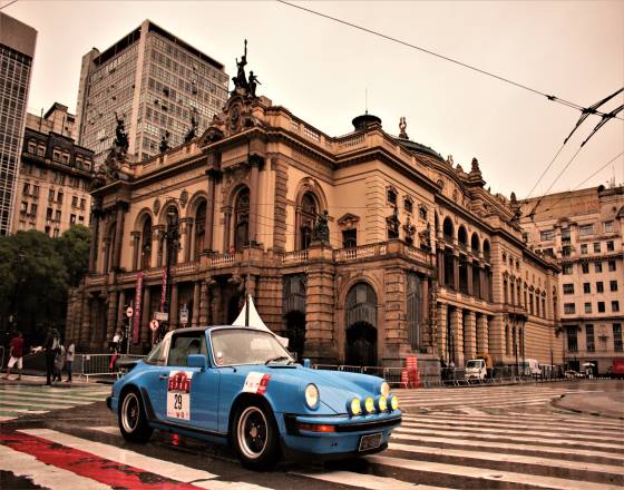 Na faixa de pedestres lateral ao Teatro Municipal um carro antigo da cor azul está estacionado