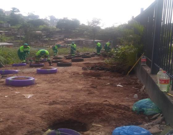 funcionários de uniformes verdes realizando plantio com mudas em pneus velhos formando um jardim
