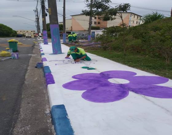 Equipe de serviços pintam os postes e as guias e nas calçadas grandes flores na cor lilás