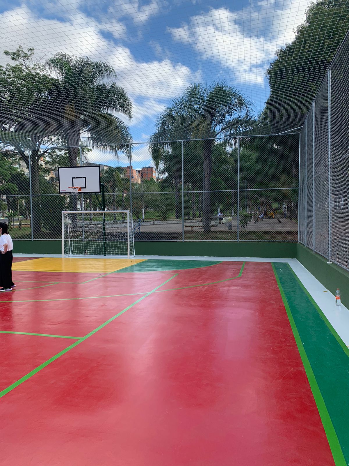 Uma quadra de esportes com a parte cimentada pintada nas cores vermelho, verde e amarelo.