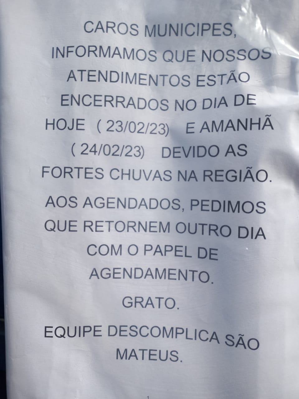 Aviso colado no portão informa: caros munícipes, informamos que nossos atendimentos estão encerrados no dia de hoje (23?02) e amanhã (24/02), devido às fortes chuvas na região. Aos agendados, pedimos que retornem outro dia, com o papel de agendamento. Frato. Equipe Descomplica São Mateus. 