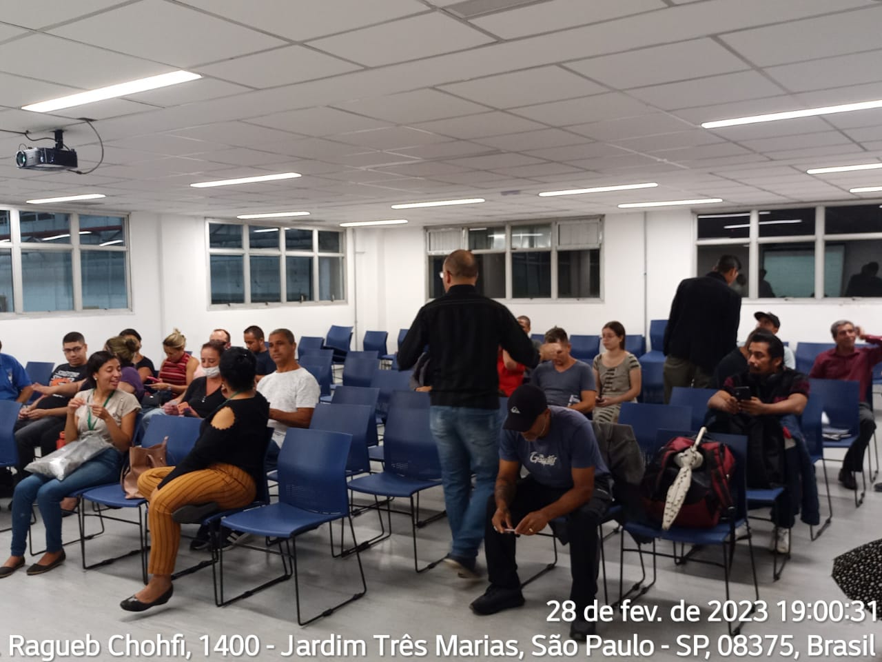 Participantes de reunião estão sentados em cadeiras azuis em um salão. Foto identificada com data de 28 de fevereiro,  Av. Ragueb Chohfi, 1.400