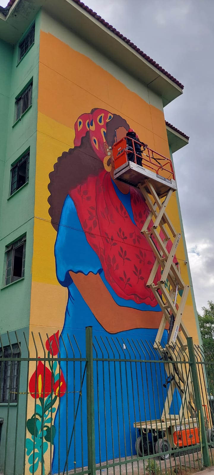 Pintora  finaliza desenho de uma mulher de vestido azul, com lenço vermelho em parte dos cabelos pretos.  c