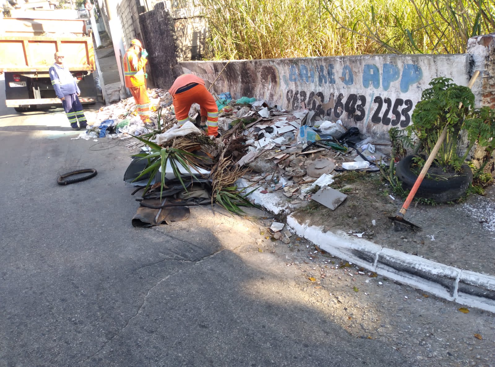 Funcion´parios da Prefeitura recolhem lixo, pedaços de madeira e plastico jogados em cima de uma calçada. 