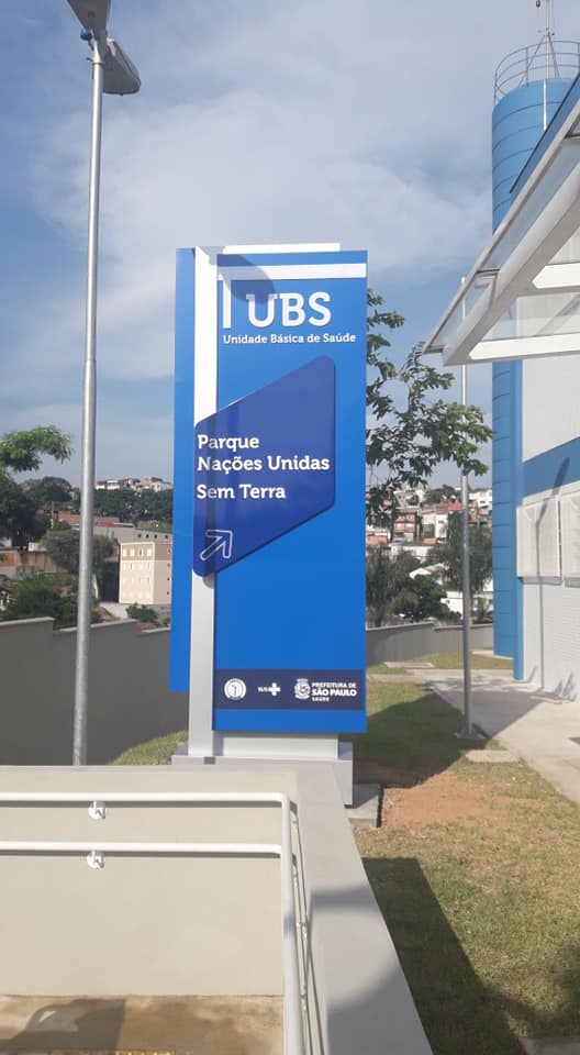  Mostra a placa de identificação da UBS, na cor azul, com os dizeres de cor branca: UBS - Unidade Básica de Saúde, Parque Nações Unidas Sem Terra