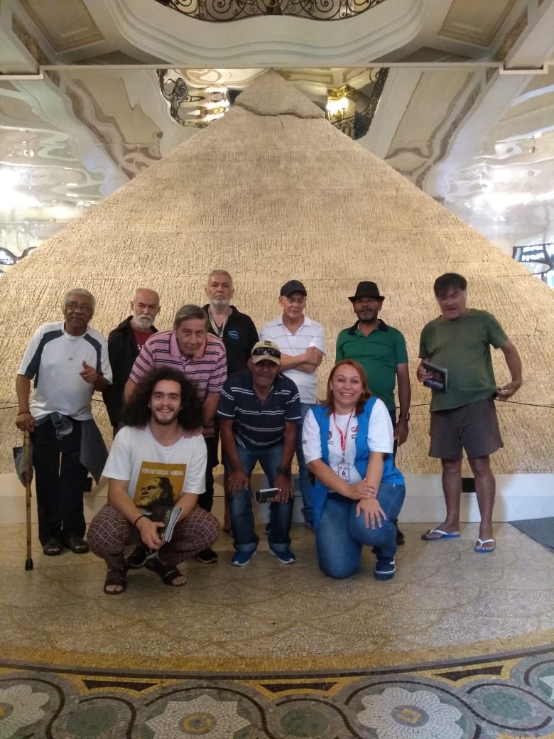 Dez pessoas posam em frente a uma imitação de uma pirâmide.