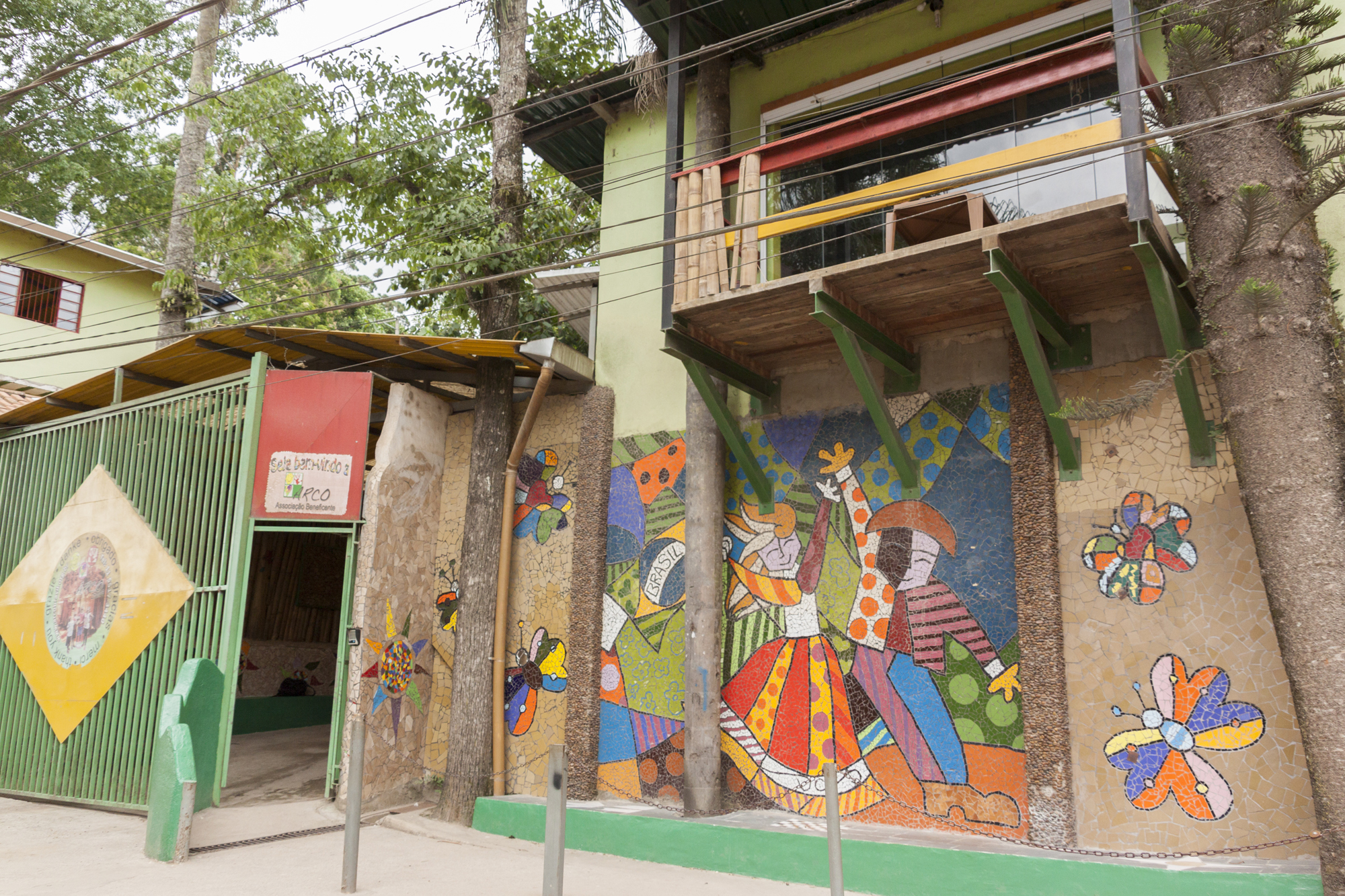 Fachada da Instituição beneficente decorada com mosaicos coloridos. Em cima da porta a esquerda, um letreiro escrito “Sejam bem vindos a ARCO”.