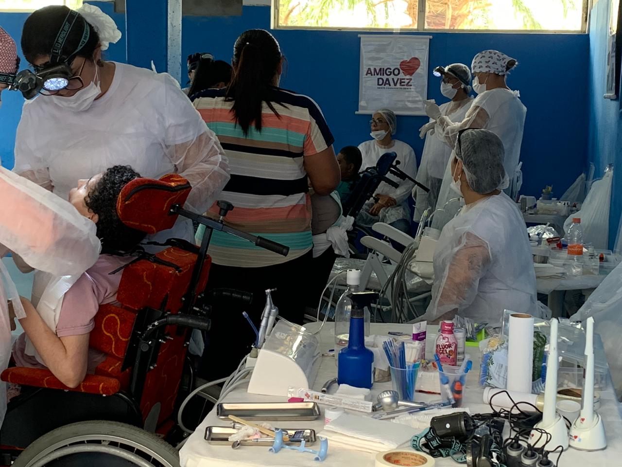 em um dos espaços da instituição Lar Ternura, mais de dez pessoas na foto. Em uma maca, uma pessoa com deficiência é atendida pela equipe de dentistas, mais de 3 pessoas ao redor.