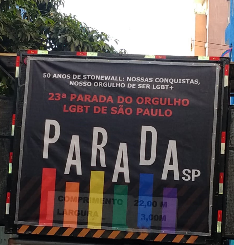 Arte oficial da vigésima terceira Parada do orgulho LGBT de São Paulo com os dizeres, cinquenta anos de Stonewall, nossas conquistas, nosso orgulho de ser LGBT+, em traseira de caminhão