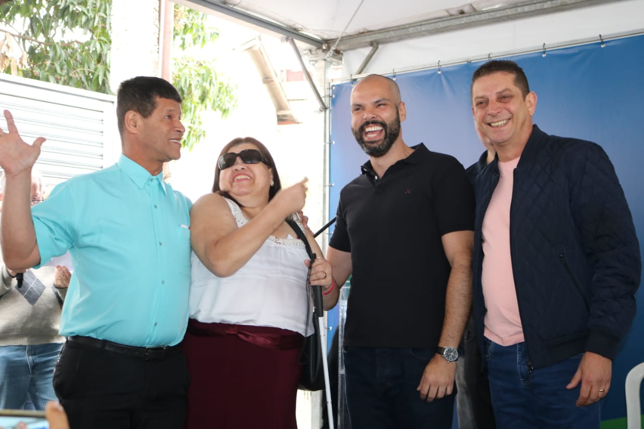 Na imagem, a foto de dois deficientes visuais recebendo a chave do apartamento das mãos do prefeito e secretário municipal de Habitação.