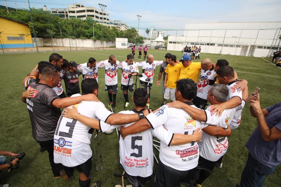 mais de vinte jogadores reunidos. Eles estão em um campo de futebol com gramado e aberto. Sorriem e seguram faixas.