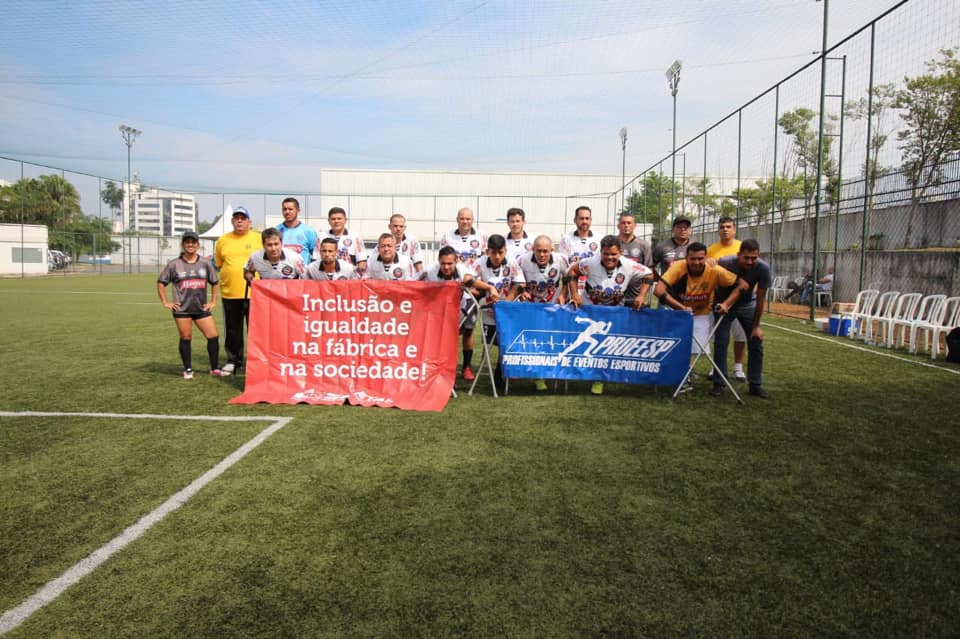 mais de vinte jogadores reunidos. Eles estão em um campo de futebol com gramado e aberto. Sorriem e seguram faixas