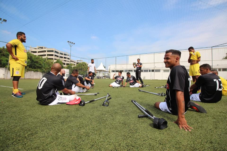  mais de dez jogadores reunidos. Eles estão em um campo de futebol aberto e com gramado. Fazem o aquecimento. 