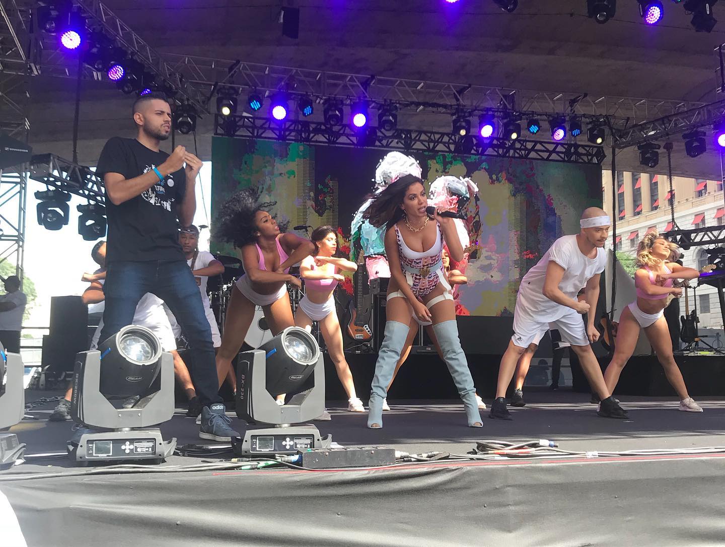 mais de dez pessoas no palco, entre elas a cantora Anitta com a banda e os dançarinos. Lado esquerdo, nosso intérprete de libras. 