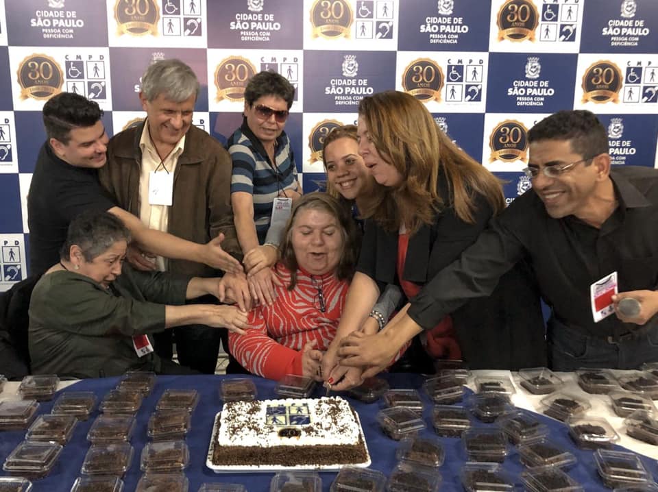 Oito pessoas unidas para cortar o bolo do aniversário de 30 anos do Conselho Municipal da Pessoa com Deficiência.