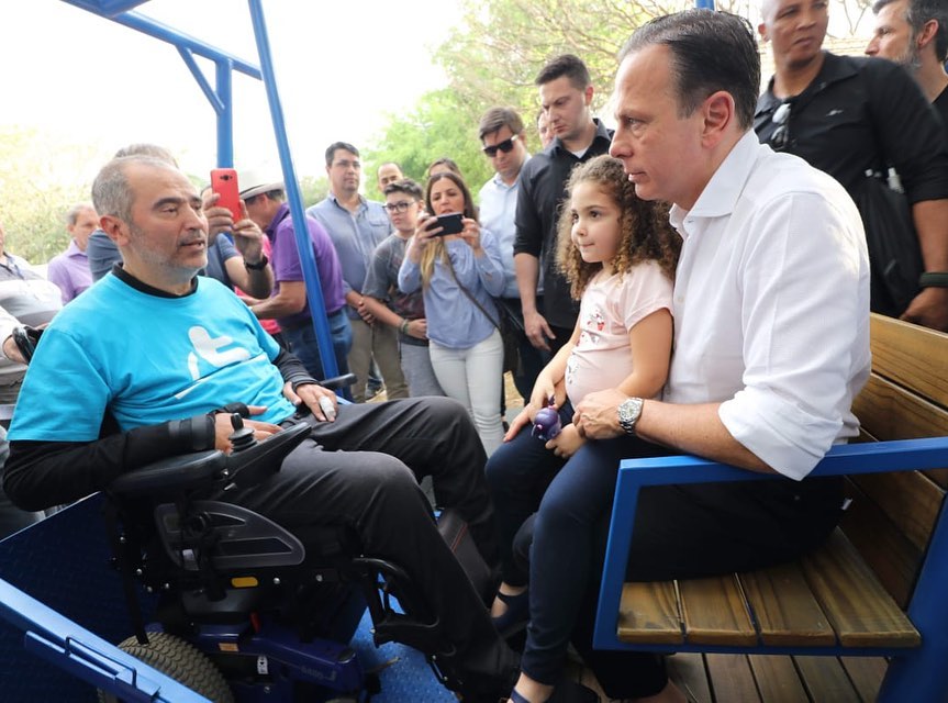 mais de quinze pessoas na foto. Dentro de um balanço, Governador João Doria com uma criança sentada no seu colo e o secretário Cid Torquato. 