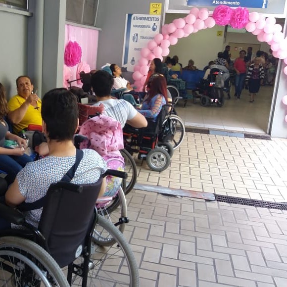 mais de quinze mulheres na entrada do hospital. Um arco de bexigas, na cor rosa, na entrada do hospital. 