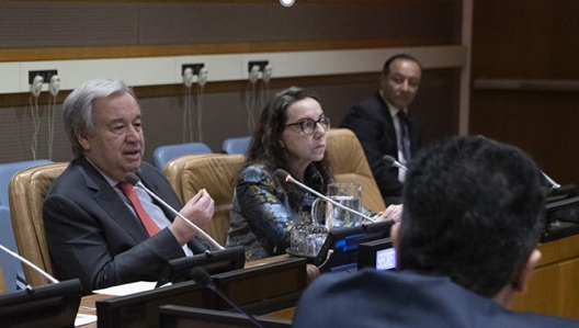 quatro pessoas na foto, entre elas o secretário geral da ONU atrás de uma mesa e com um microfone. Ele discursa.
