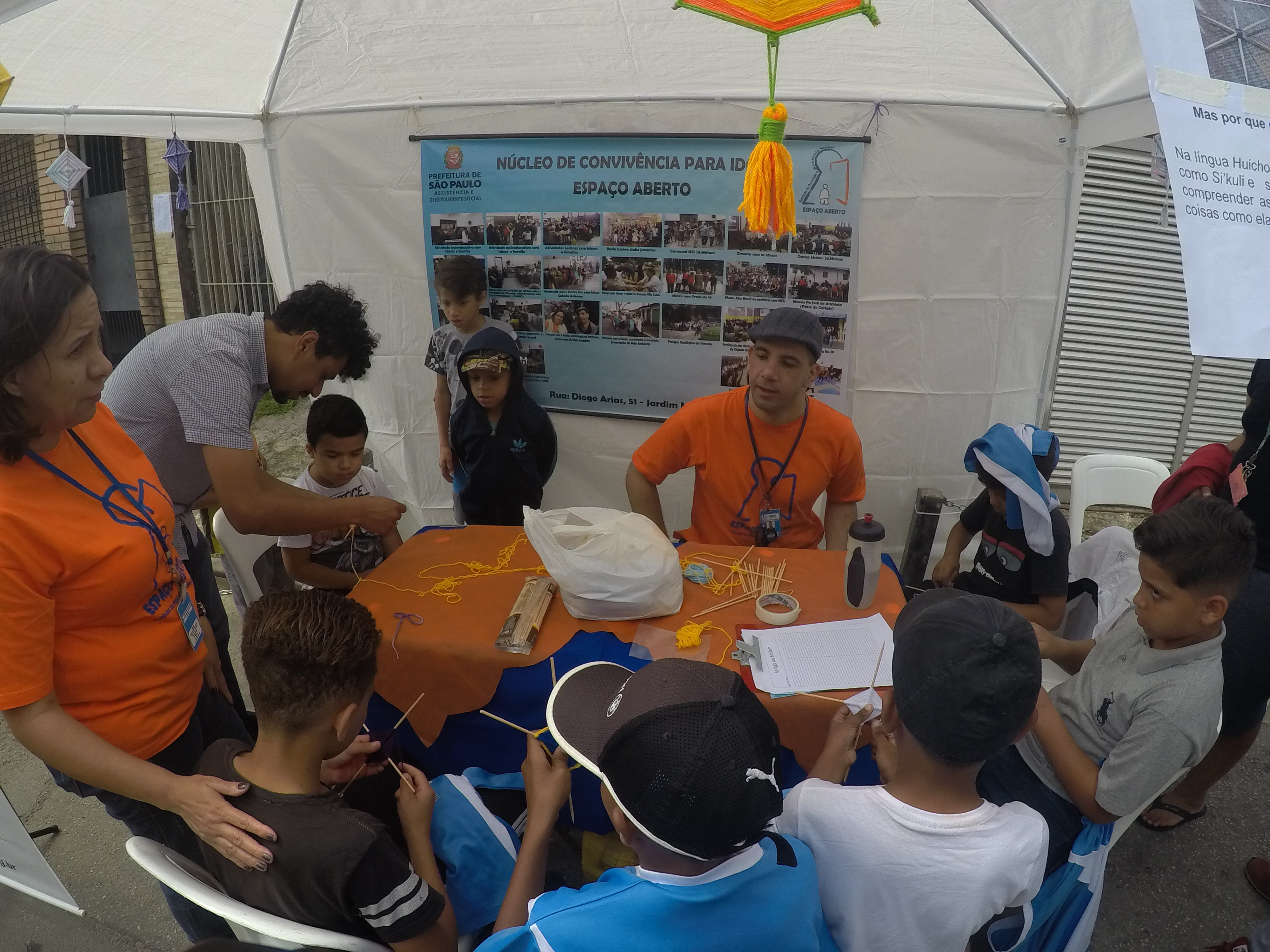 Dentro de uma tenda no evento, crianças estão com orientador realizando artesanato