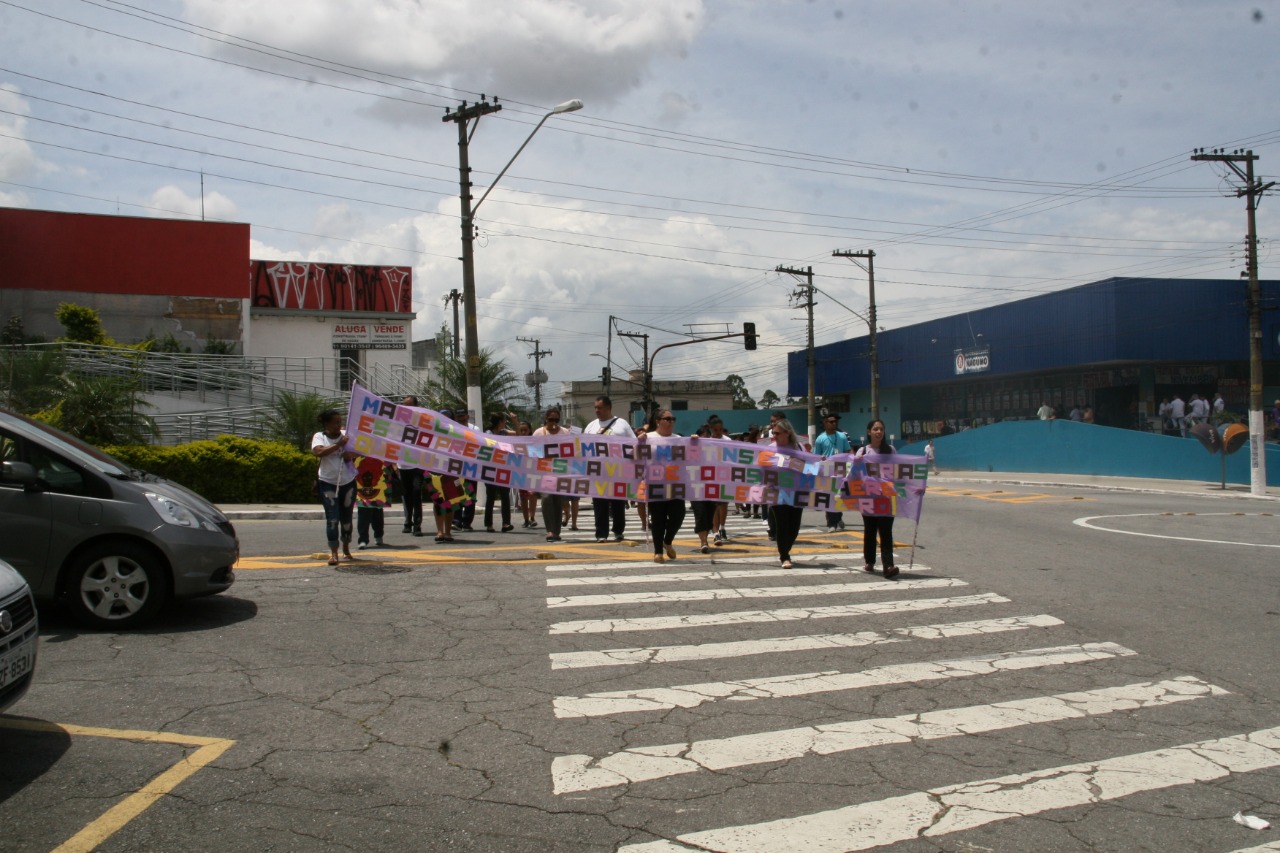Atravessando a rua, pessoas caminham com faixas em prol dos direitos da mulher e a não violência