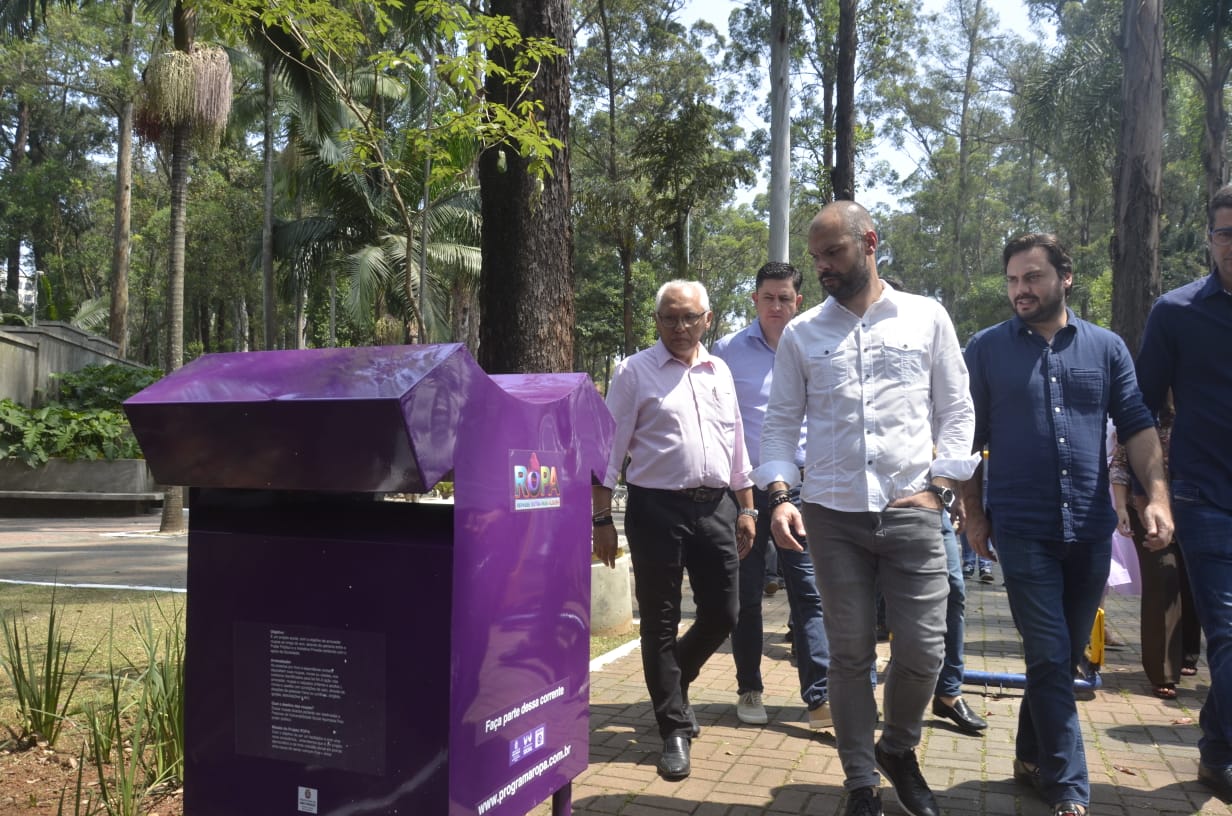 Bruno Covas, Filipe Sabará e outras autoridades caminham pelo parque ao lado do coletor de roupas do programa