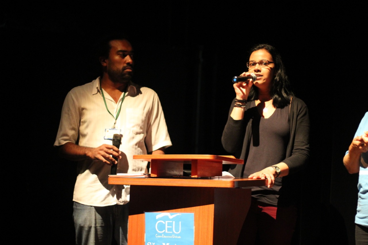 Duas pessoas em frente ao palco discursando durante o seminário