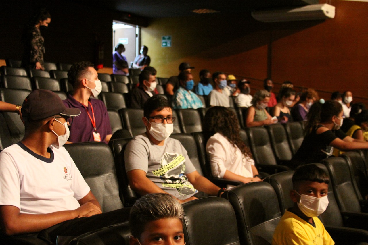 Crianças e adolescentes de mascaras espalhadas pelo teatro para a exibição do filme 