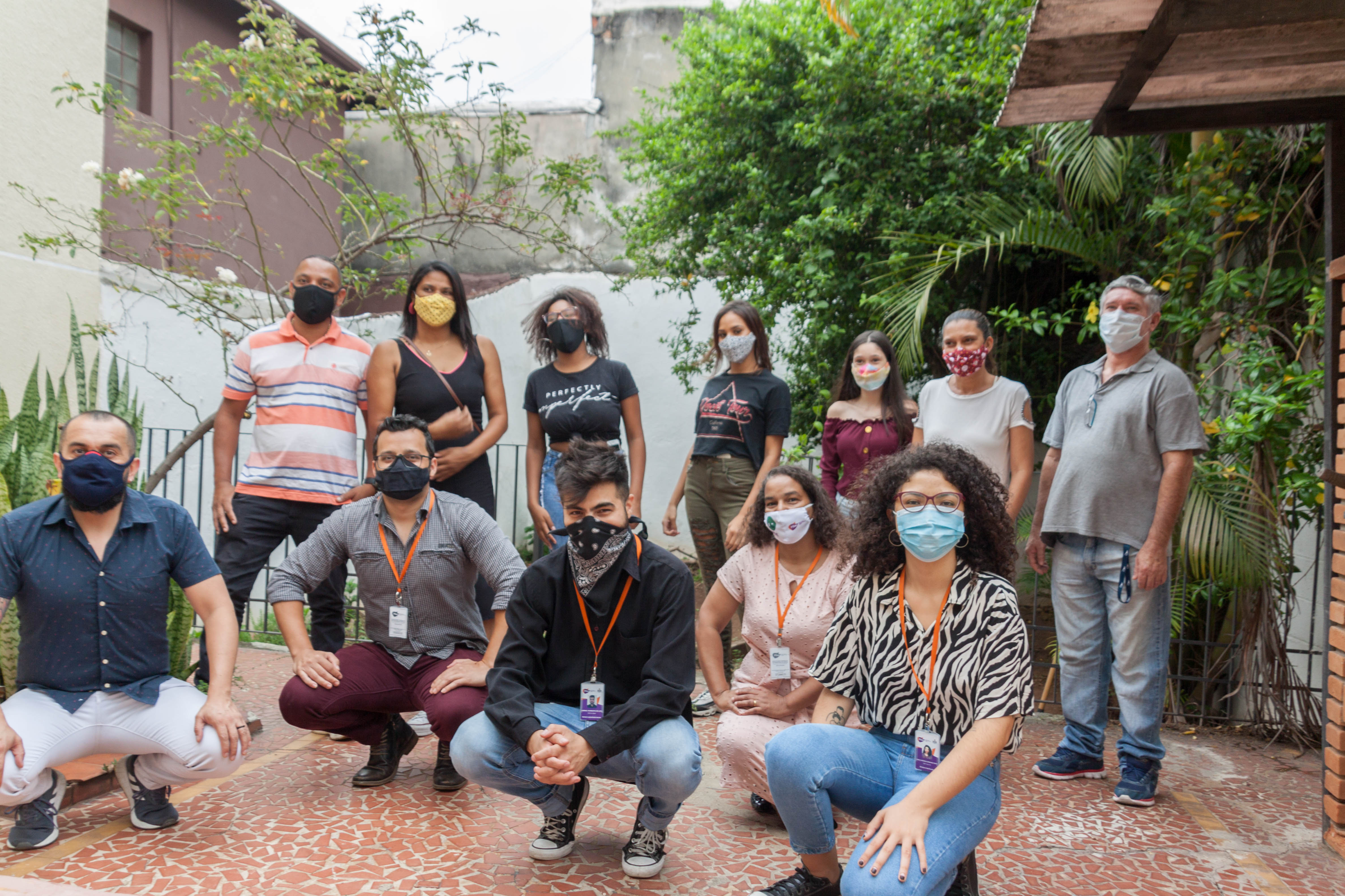 Doze pessoas posam para foto. Todas usam máscara e estão distanciadas umas das outras e também separadas em uma fileira de 8 pessoas em pé e as demais 4 pessoas agachadas.