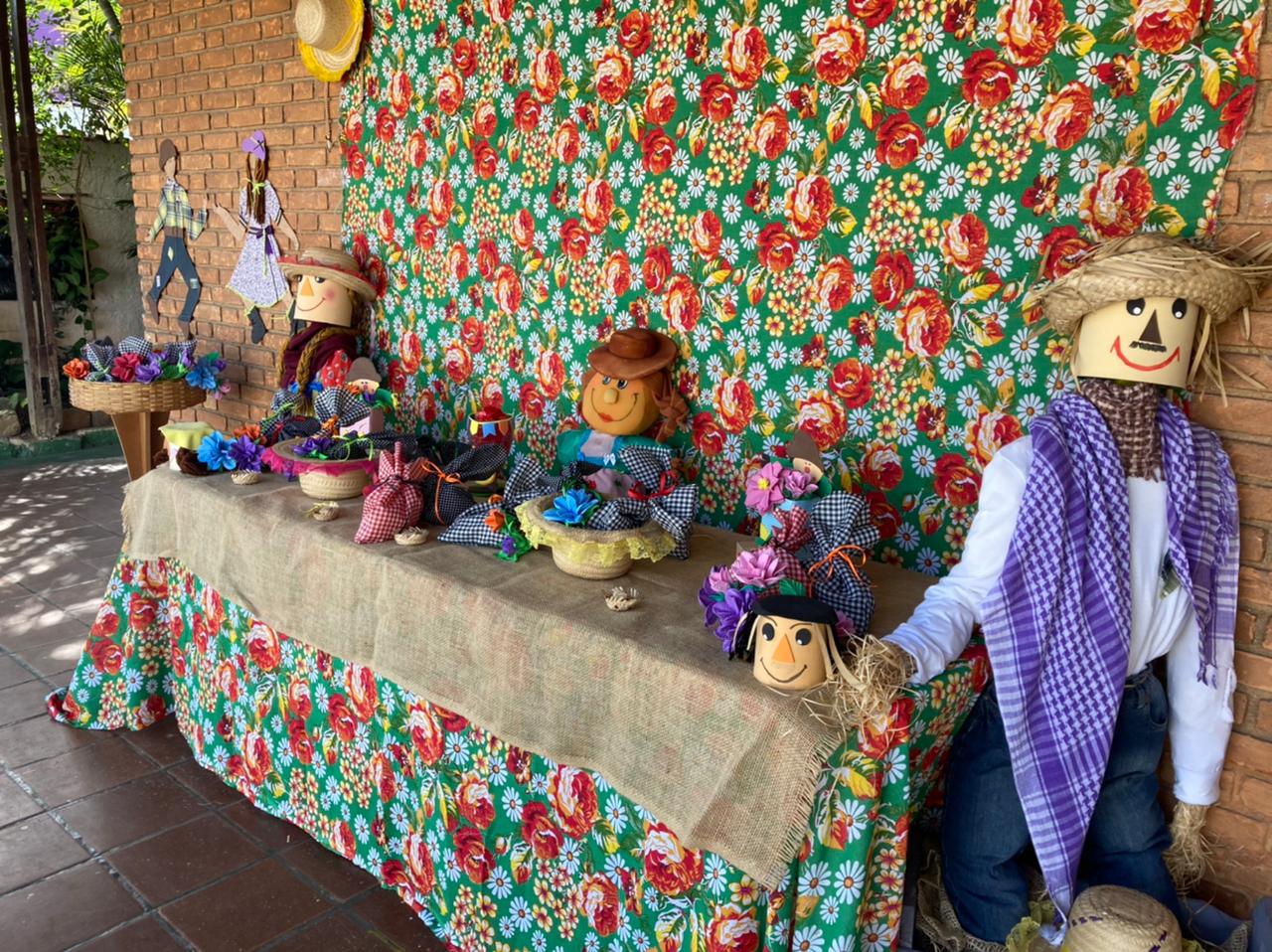 Mesa decorada com estampas características de festa junina, saquinhos de doces, bonecos com chapéus de palha e roupas típicas da festa.