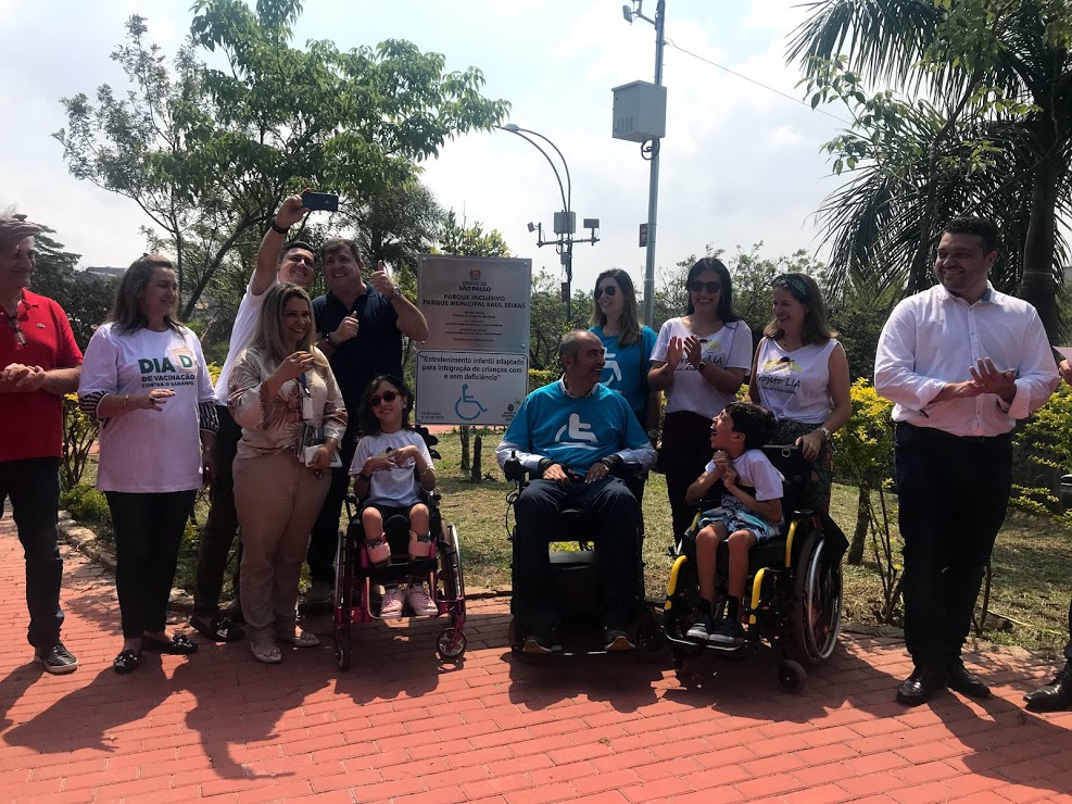 mais de dez pessoas ao redor da placa de inauguração do Parquinho Inclusivo, entre elas o secretário Cid Torquato com Manu, Gabriel e suas mães do Projeto Lia.