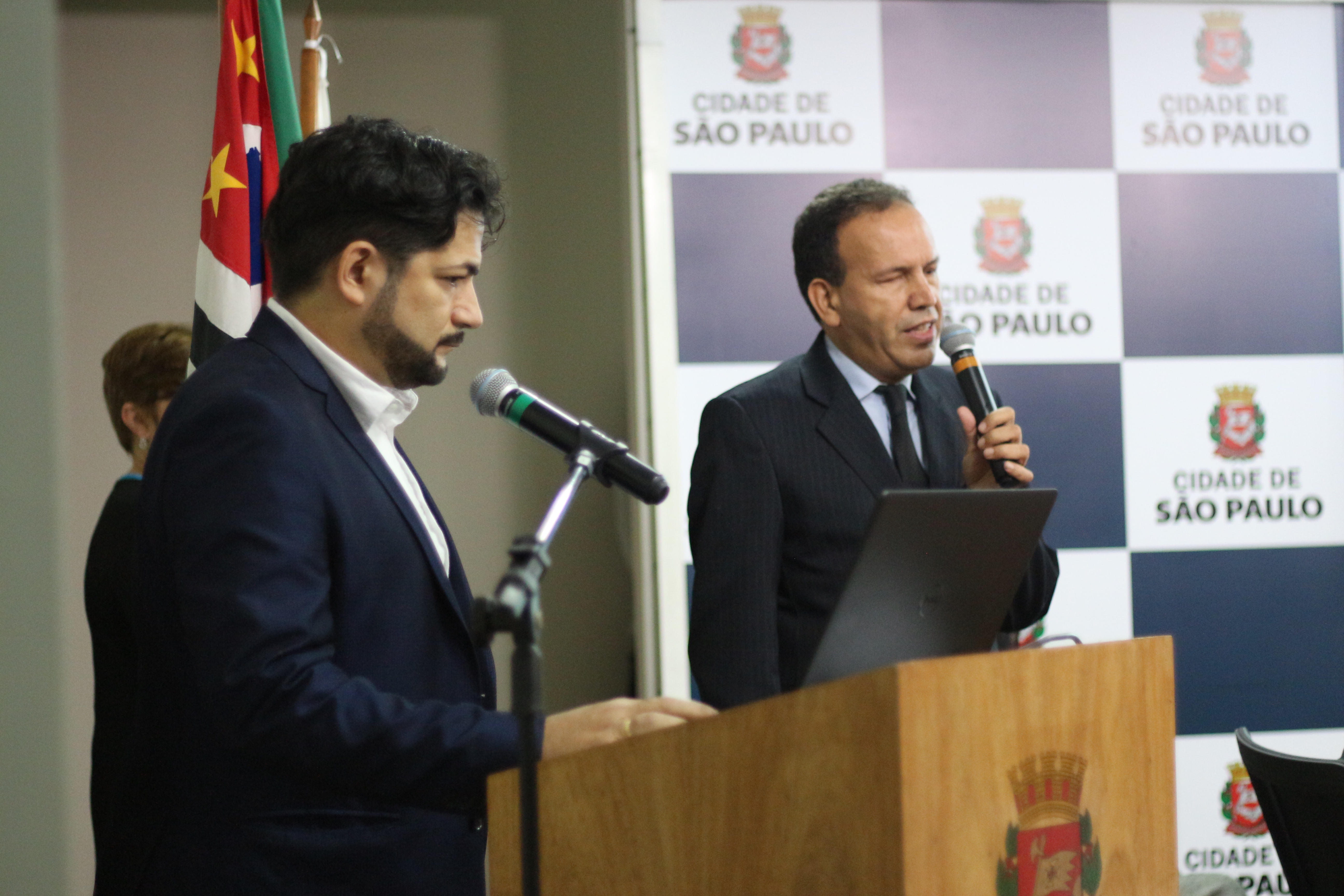 três pessoas na foto. No palco e no microfone, Sidney Tobias analista de sistemas da Prodam e consultor de acessibilidade digital da SMPED. 