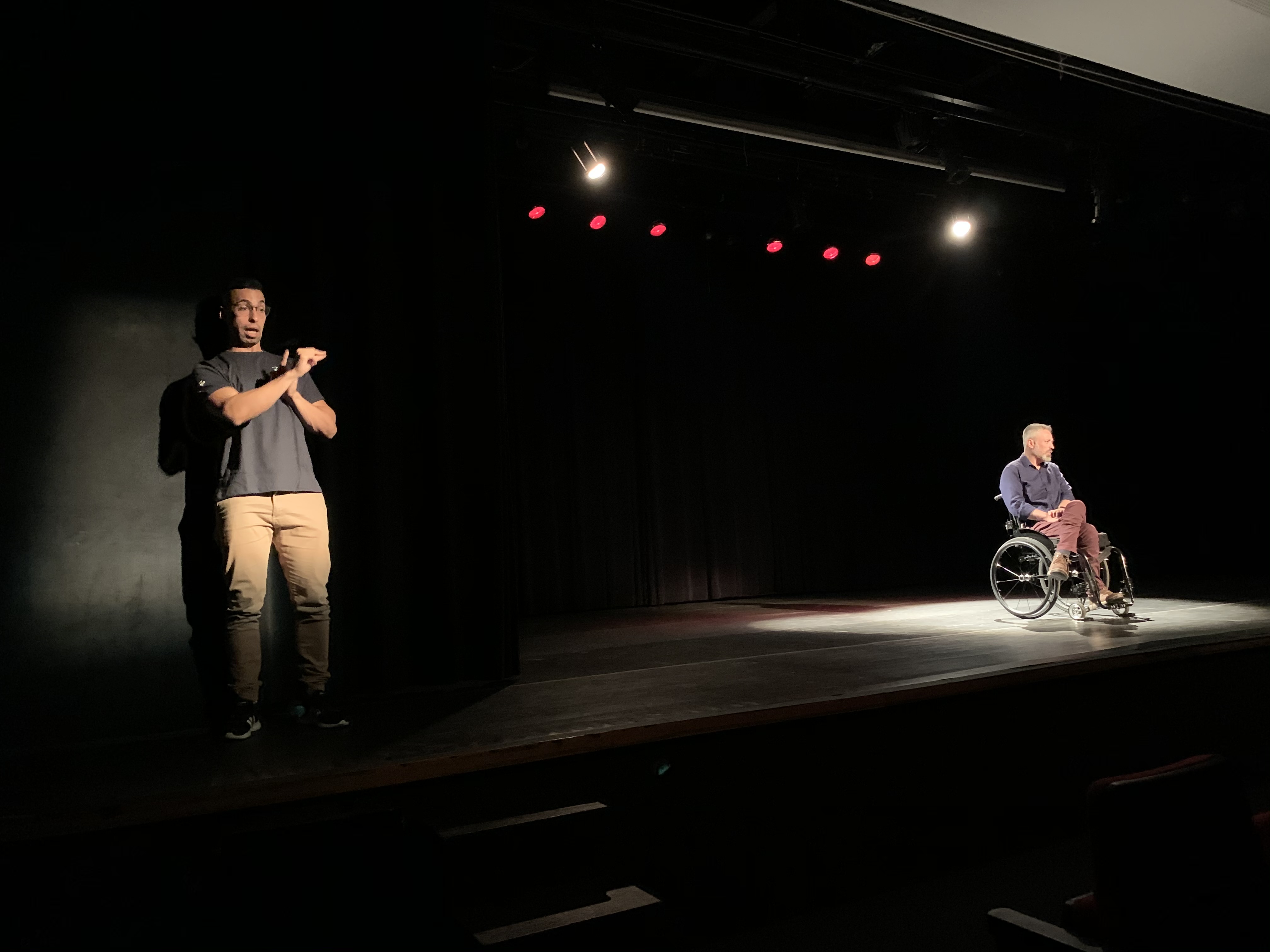 #PraCegoVer: Um homem em uma cadeira de rodas se apresentando em um palco, ao lado esquedo um interprete de libras.