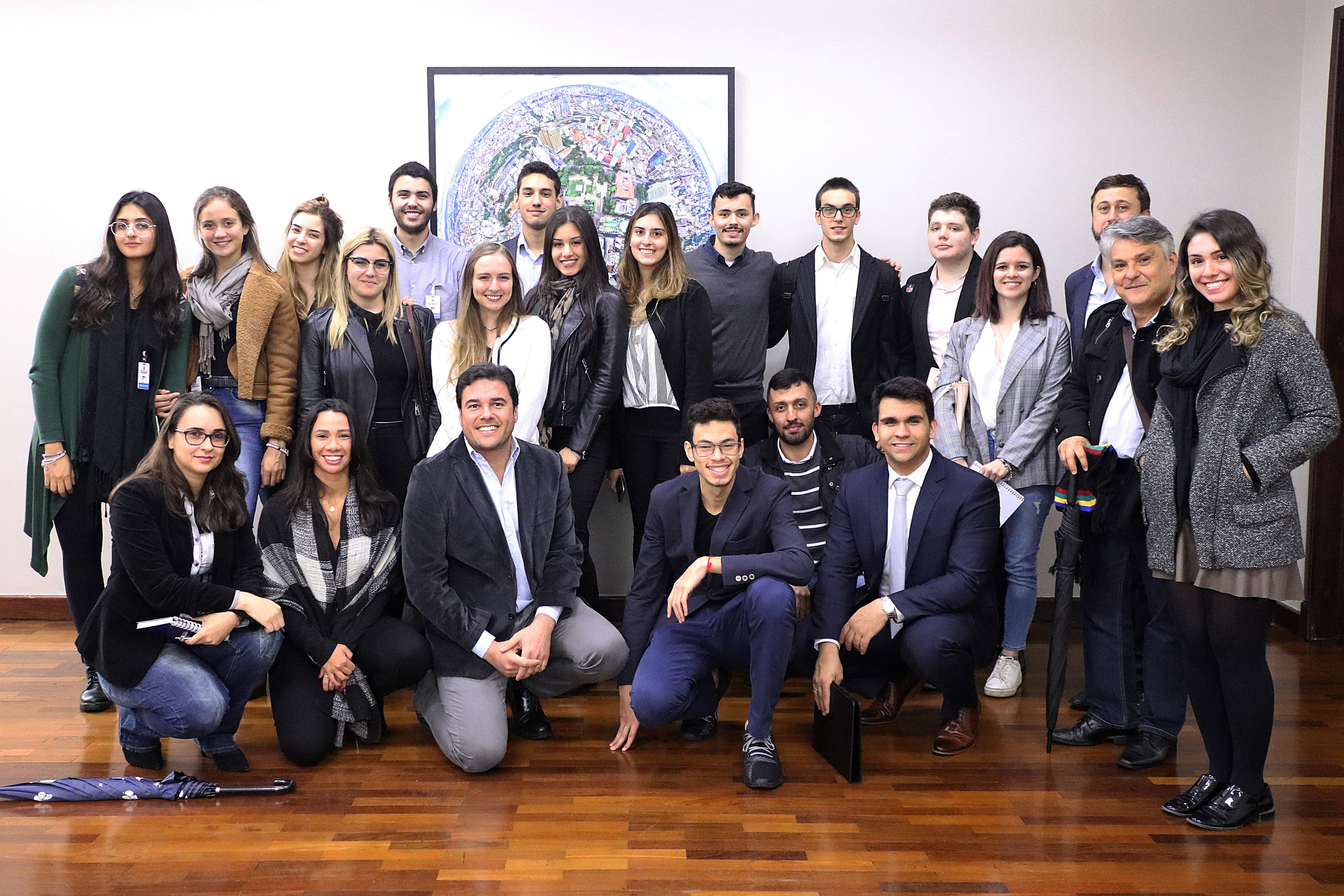 Alunos do Instituto Brasileiro de Mercado de Capitais posam ao lado do Secretário Luiz Alvaro. Ao fundo, um quadro fotográfico da cidade de São Paulo.
