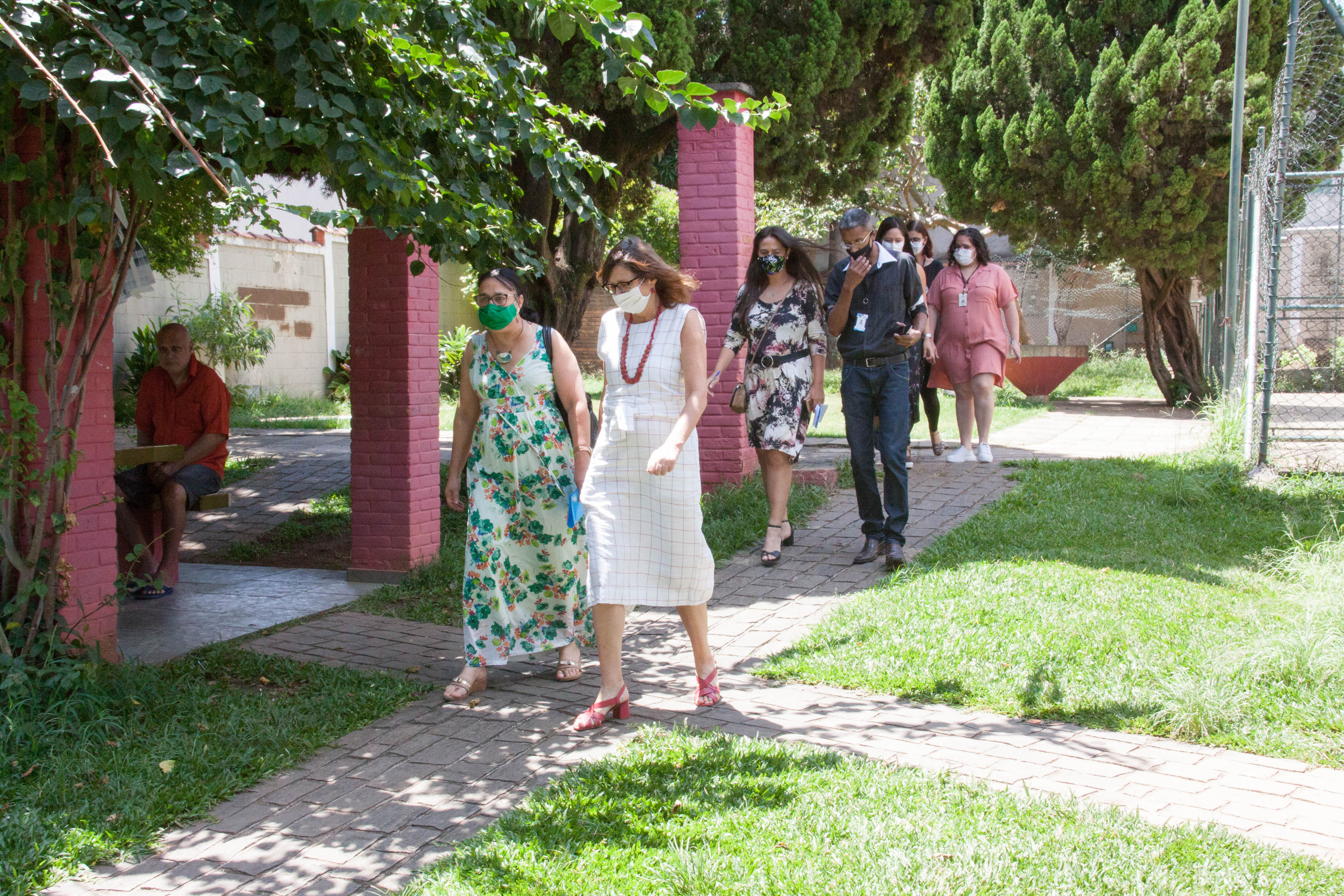 Secretária Berenice Giannella e equipe visitam o jardim do CAE Família Penha. O gramado possui um caminho de pedras assentadas e colunas de tijolinho vermelho.