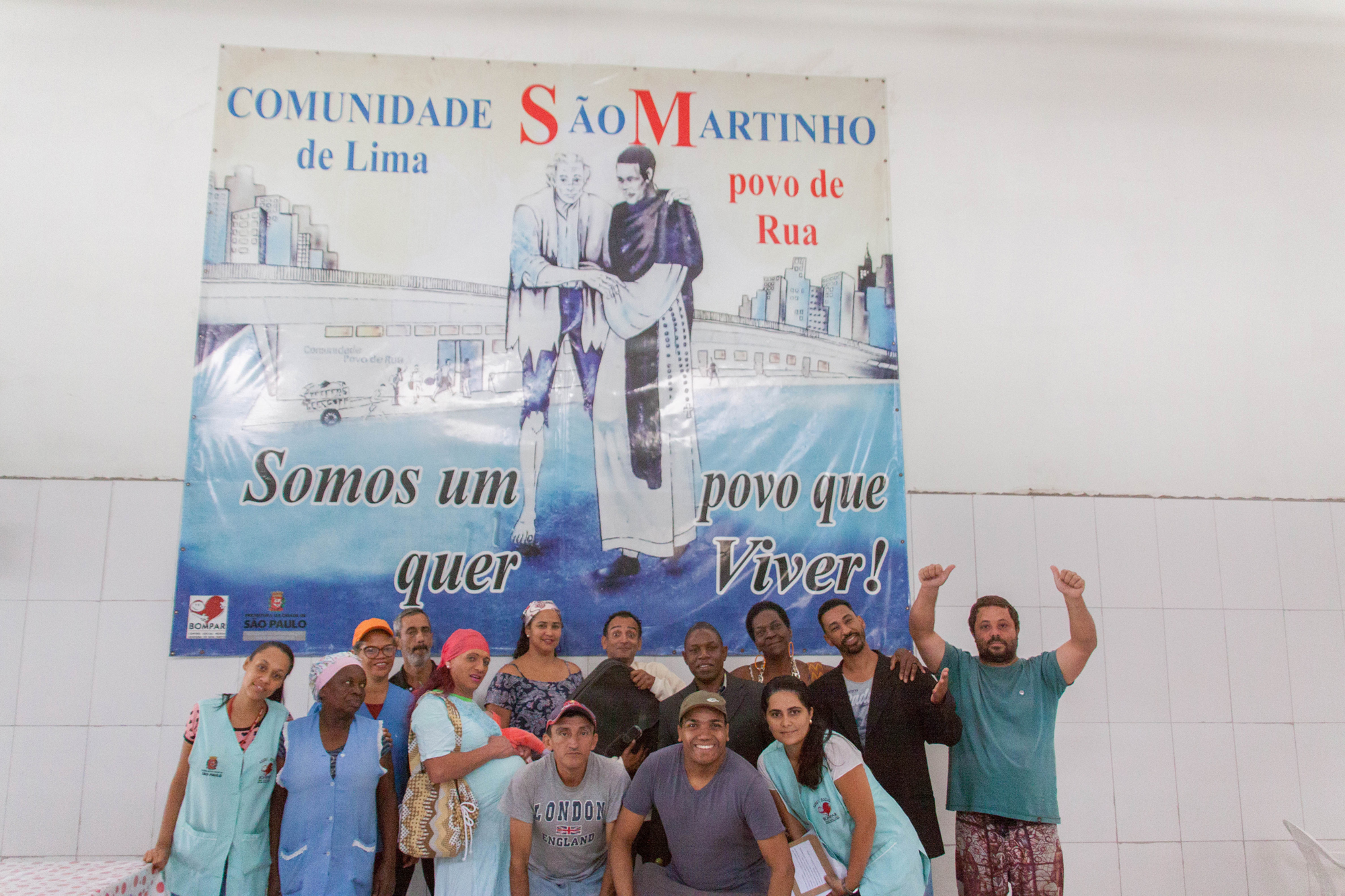 Conviventes e funcionárias posam para foto junto com mural da Comunidade São Martinho de Lima