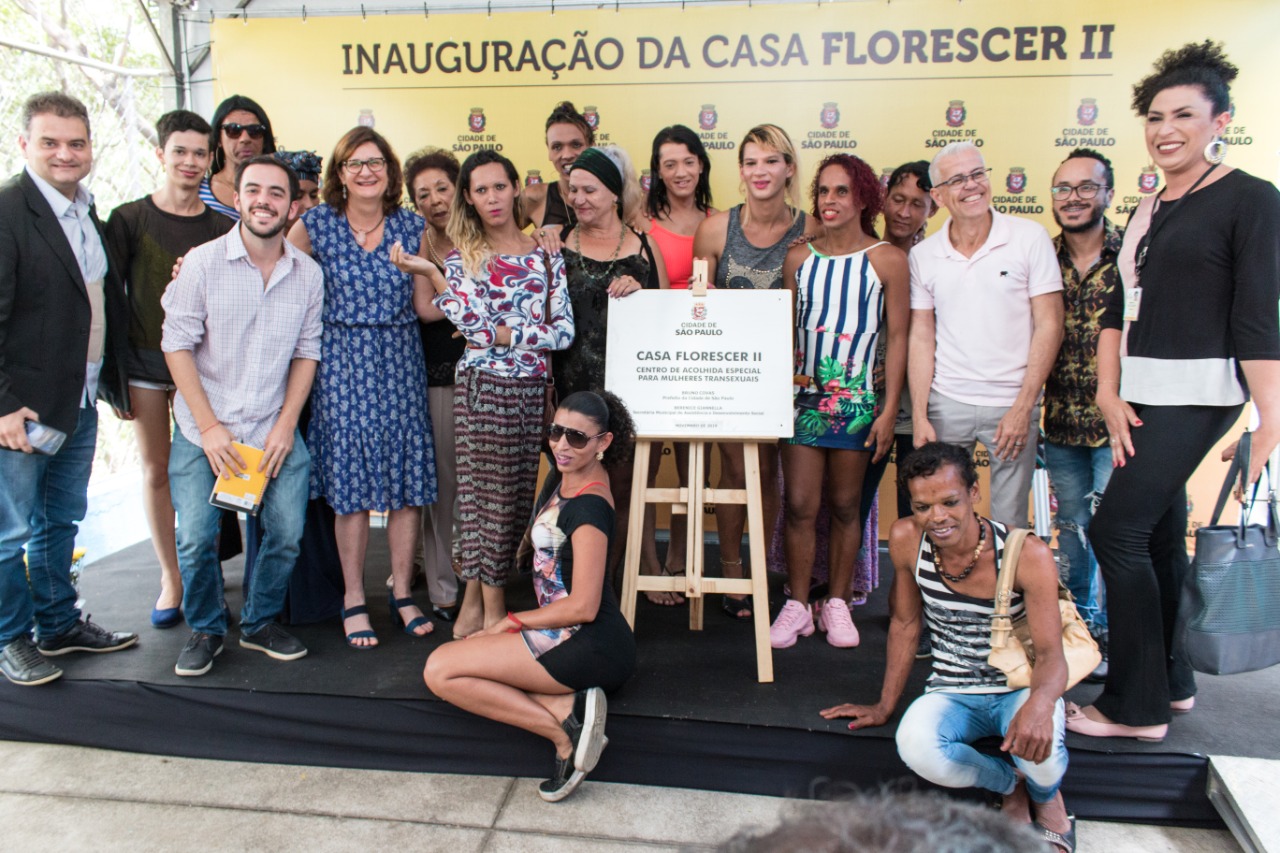 No palco, com a placa de aço de inauguração do novo serviço, a secretária municipal de Assistência e Desenvolvimento Social, Berenice Giannella e o secretário adjunto, Marcelo Del Bosco, e outros convidados posam para foto com as conviventes da Casa Florescer II. 