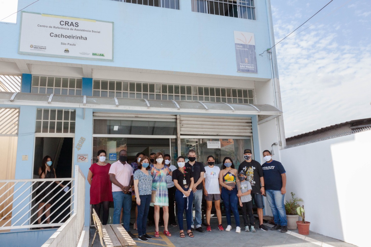 Fachada do CRAS Cachoeirinha reformado. Sobrado na cor azul clara com grades brancas nas janelas. Em frente à entrada, alguns funcionários e convidados posam para a foto.