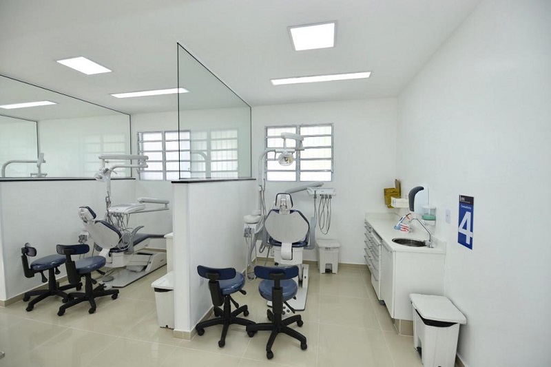 #PraCegoVer: Sala grande com duas divisórias. Em cada divisória há uma cadeira de dentista e aparelhos para atendimento odontológico. A sala é muito bem iluminada, e suas paredes são brancas.